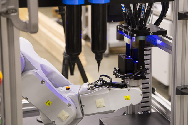 A six-axis robot transfers medical parts between adhesive dispensing, curing and vision inspection